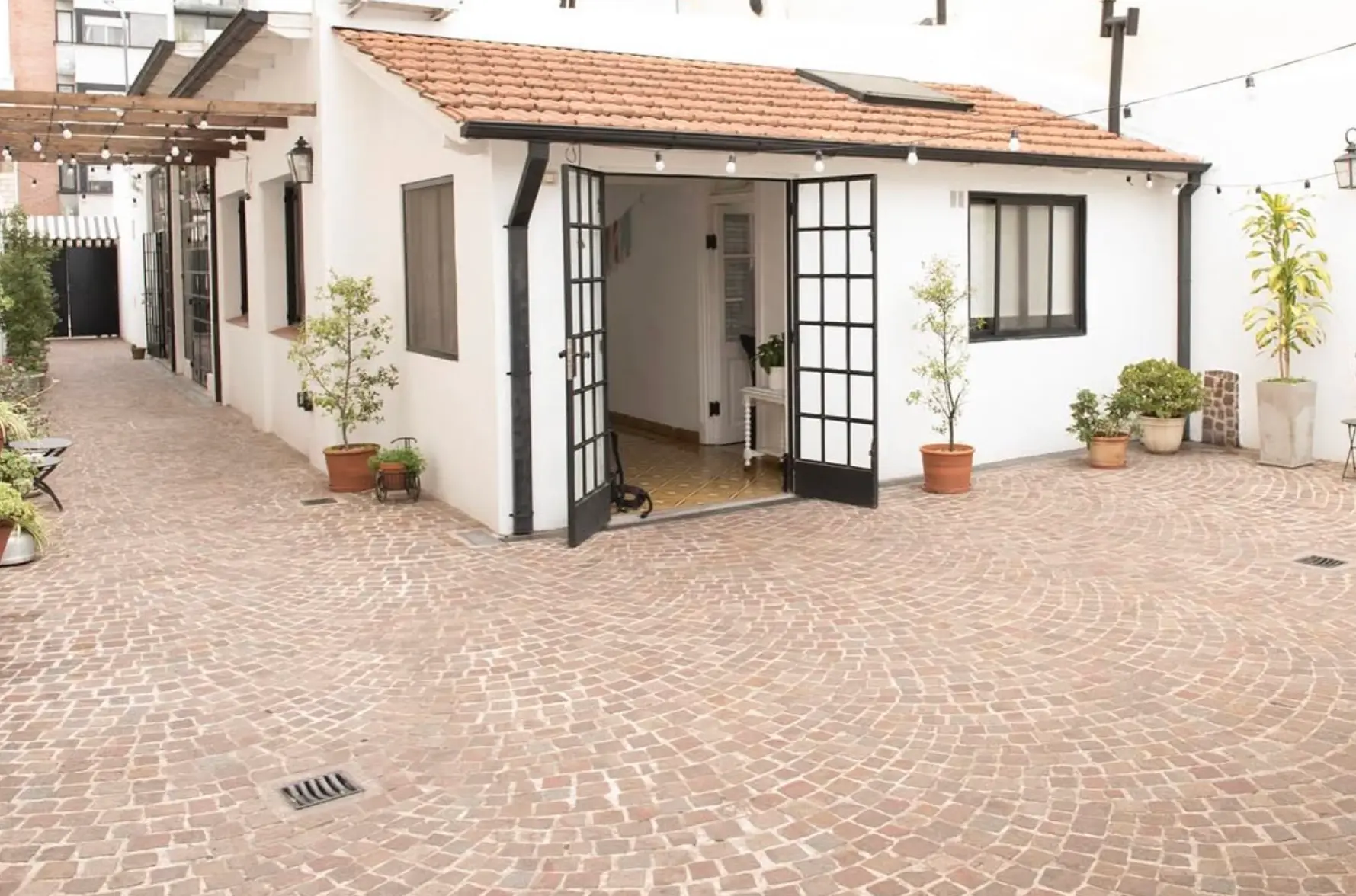 Patio empedrado de la casa con puertas vidriadas y pérgola