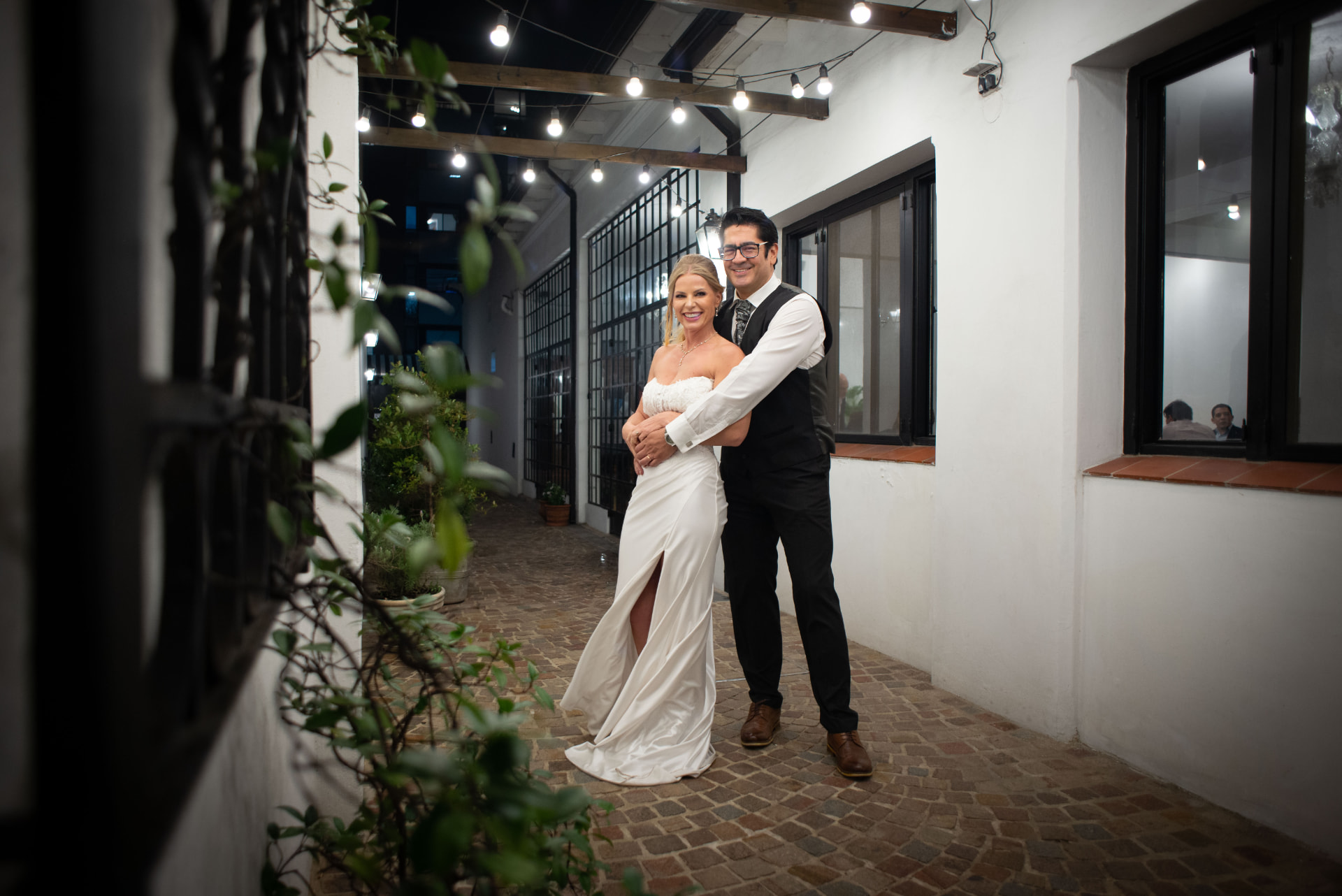 Novios abrazados en el pasillo empedrado con guirnaldas de luces