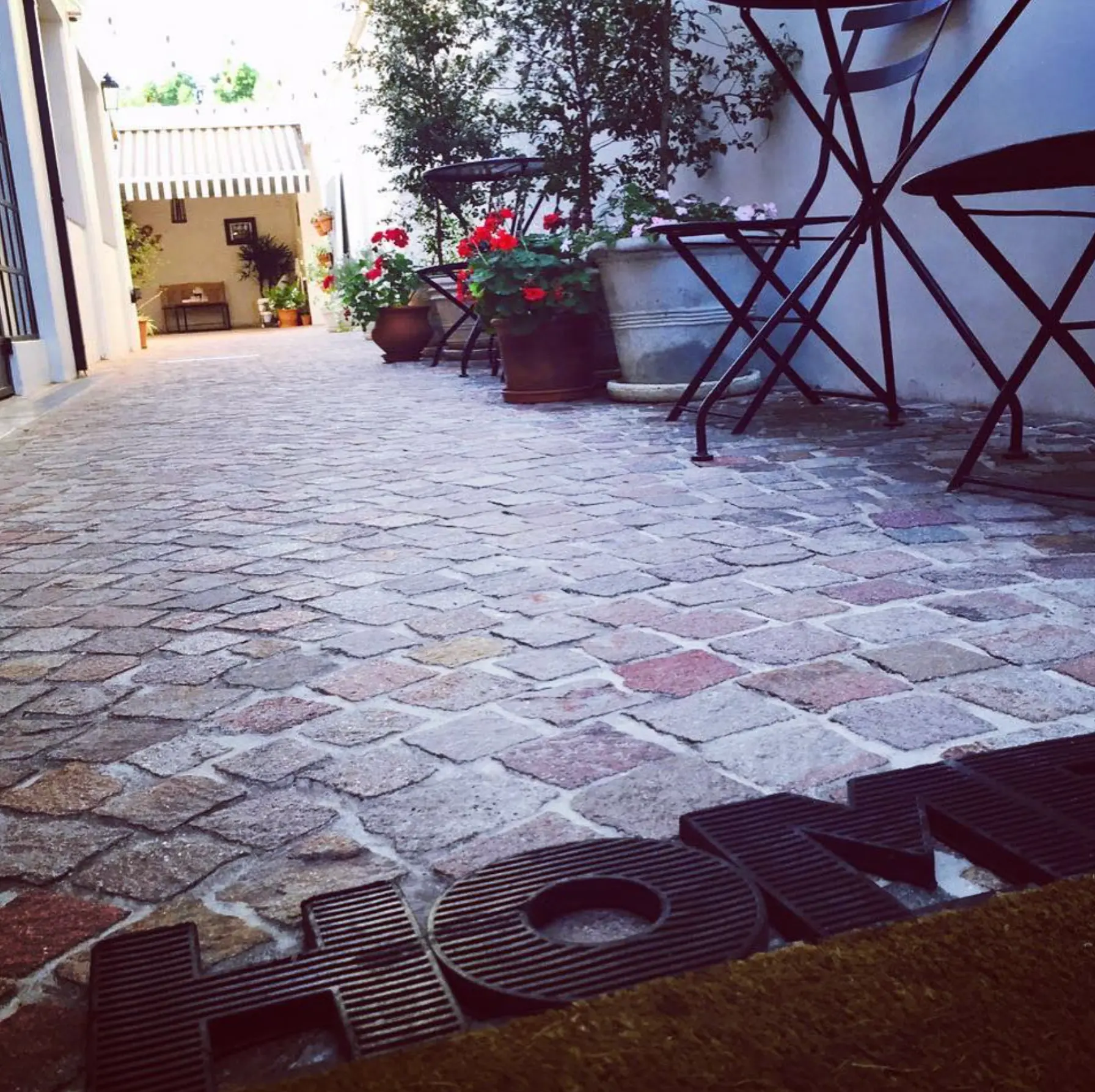 Patio de pórfido con mesas de hierro, geranios y felpudo de bienvenida