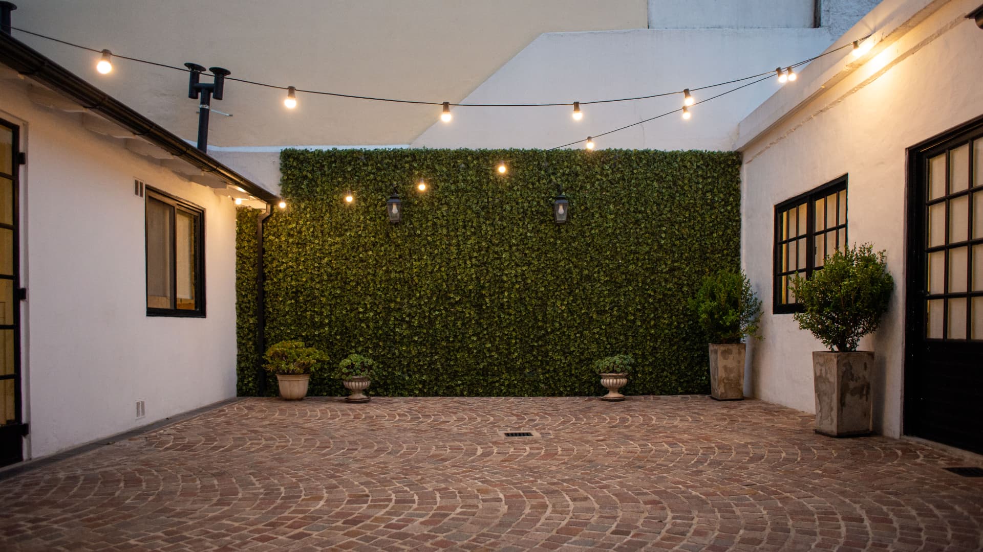 Patio de ladrillo con muro verde y guirnaldas de luces
