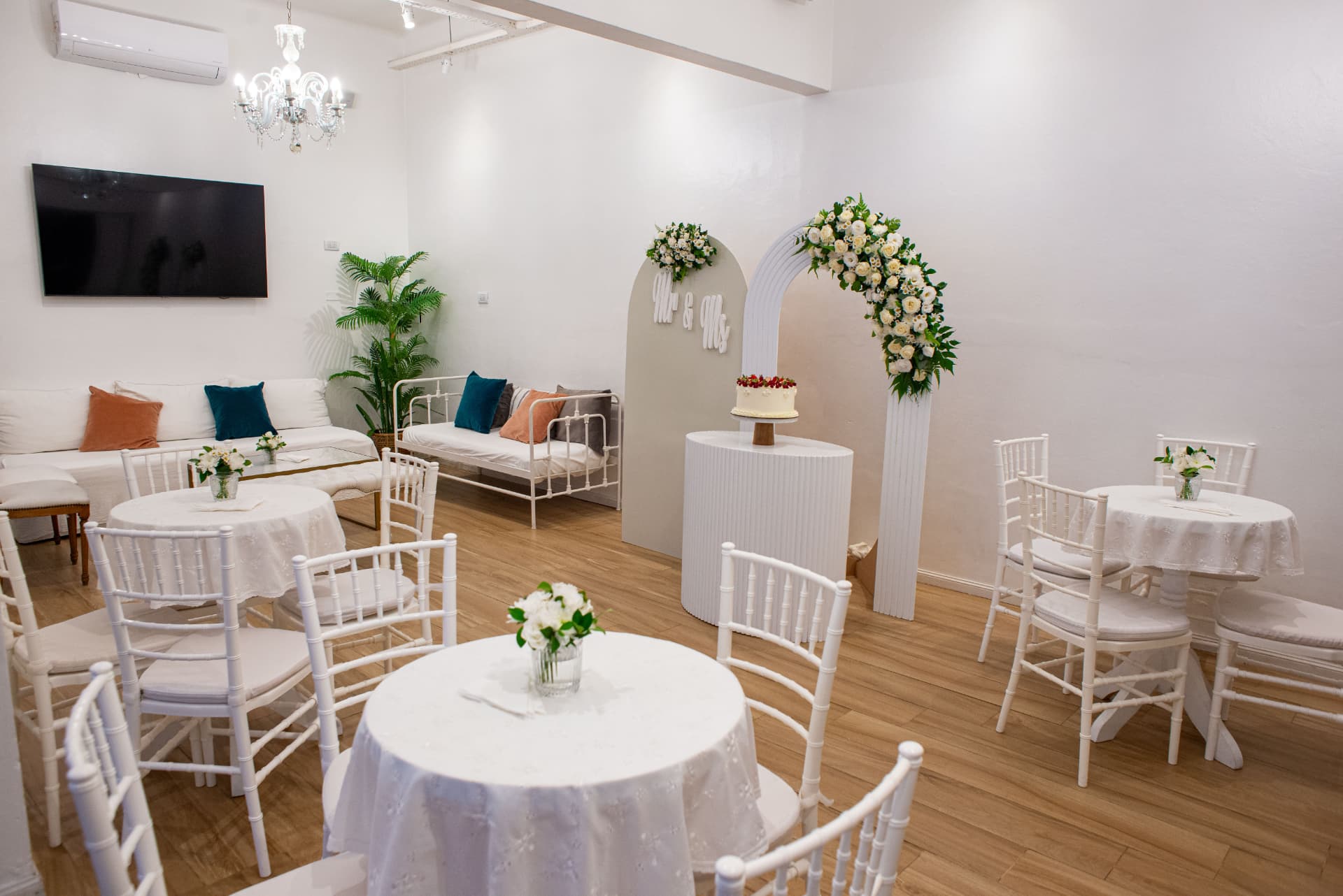 Salón montado con mesas redondas, sillas Tiffany y arco floral