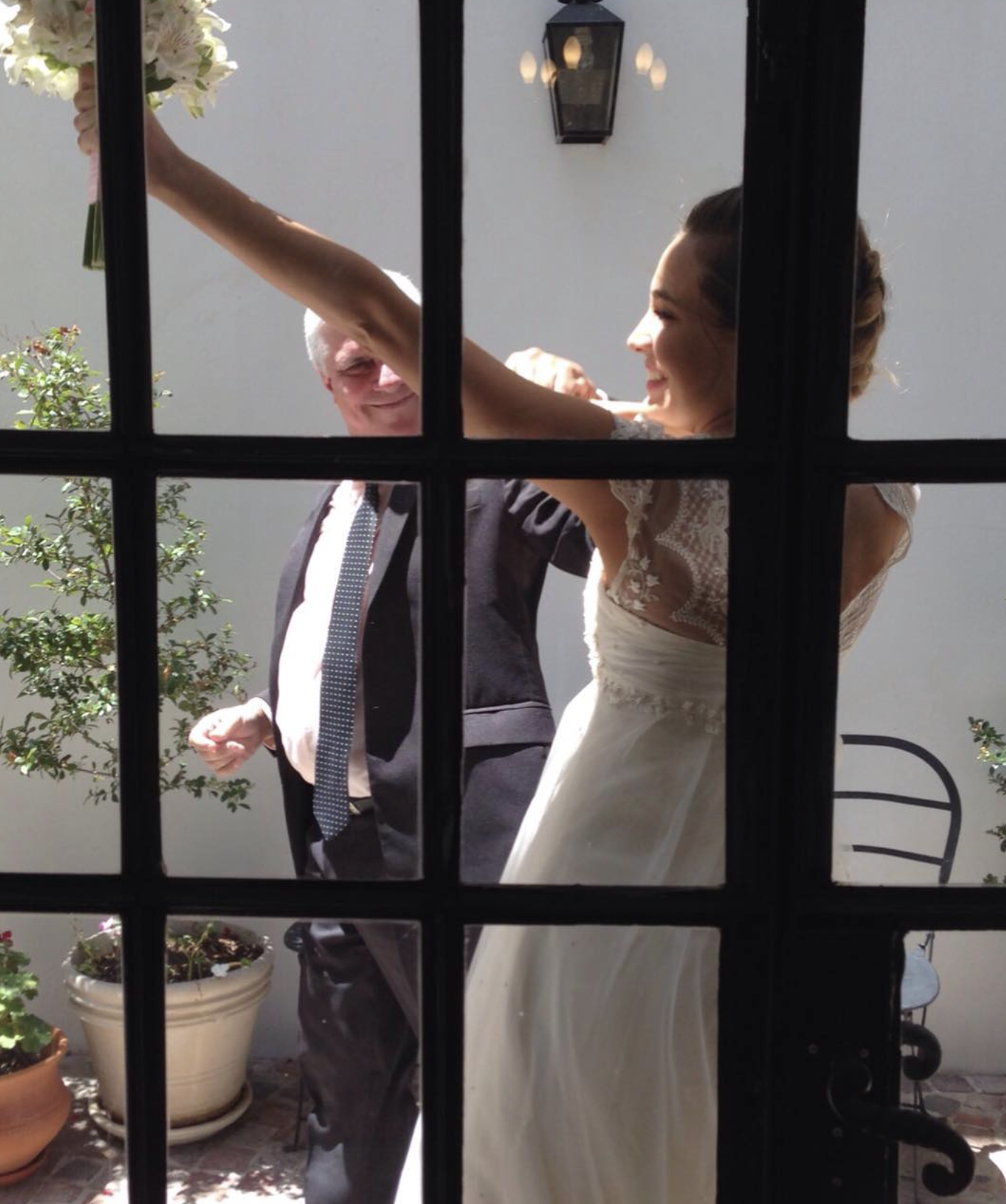 Novia y su padre entrando al patio, vistos a través de las puertas vidriadas